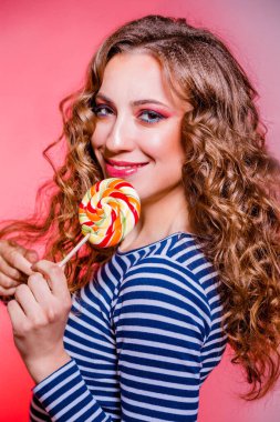 Happy beautiful brunette girl with red makeup, curly hair and a blue stripes sweater posing against a red background