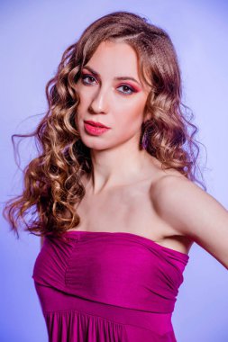Sensual beautiful brunette girl with red makeup, curly hair and a burgundy top posing on a violet background