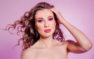 Sensual beautiful brunette girl with red makeup, curly hair and a burgundy top posing on a violet background