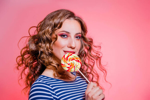 Happy beautiful brunette girl with red makeup, curly hair and a blue stripes sweater posing against a red background