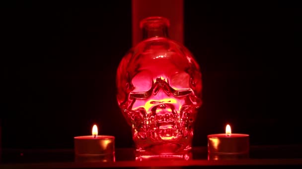 人間の形のガラスの頭蓋骨の近くで 赤いろうそくは 液体が動く赤いランプの背景に燃えています 儀式的概念 — ストック動画
