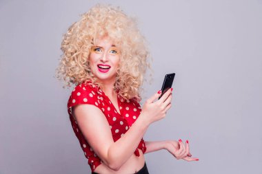 Kıvırcık saçlı, parlak sarı makyajlı ve kırmızı benekli bluzlu güzel sarışın kız kameraya dalgın bir ifadeyle bakıyor.