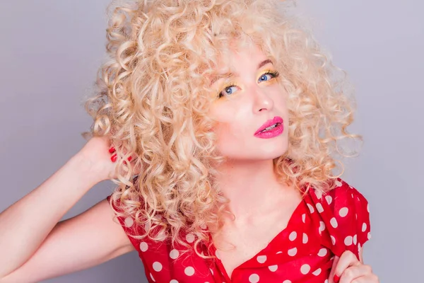 Beautiful blonde girl with a curly curly hairstyle, bright yellow make-up and red polka dot blouse looks at the camera — Stock Photo, Image