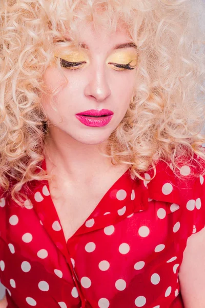 Όμορφη ξανθιά κοπέλα με σγουρό σγουρό χτένισμα, φωτεινό κίτρινο μακιγιάζ και κόκκινη πουά μπλούζα κοιτάζει την κάμερα — Φωτογραφία Αρχείου
