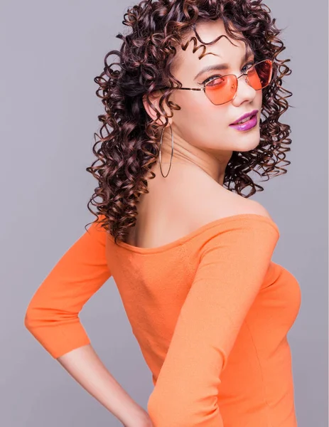 Modne brunetka dziewczyna w jasny pomarańczowy sweter i okulary pozowanie na szarym tle — Zdjęcie stockowe