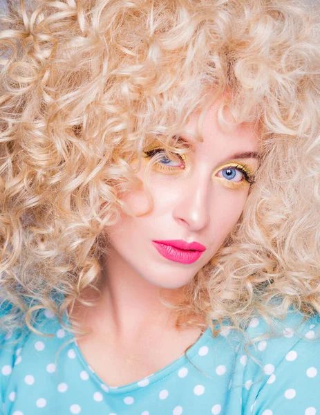 Beautiful fashionable blonde girl in retro style with voluminous curly hairstyle, in a blue polka dot blouse on a gray background looks at the camera. — Stock Photo, Image