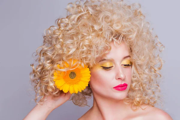 Schöne modische blonde Mädchen im Retro-Stil mit voluminöser lockiger Frisur, offenen Schultern und einer Sonnenblume in den Händen auf grauem Hintergrund. — Stockfoto