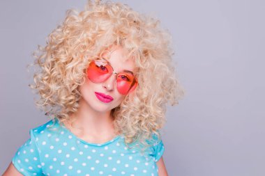 Gri bir arka planda mavi benekli bluz ve pembe gözlüklü, kıvırcık saçlı, eski tarz sarışın bir kız.