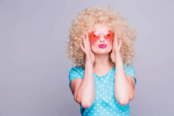 Beautiful retro-style blonde girl with voluminous curly hairstyle, in a blue polka-dot blouse and pink glasses on a gray background — Stock Photo, Image