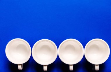 Dört boş beyaz kahve fincanı mavi arka planda bir sırada duruyor. Üst görünüm