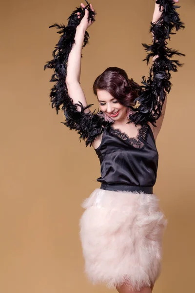 ダチョウの羽から黒いボアの中のブルネットの美しい女性はベージュの背景で踊っています 縦の写真 — ストック写真