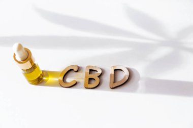 CBD yağ damlası şişesi ve CBD kelimesi beyazda izole edilmiş. Kenevir yaprağının gölgesini bırak. Yatay fotoğraf