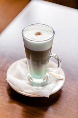 Kafedeki bir masanın üzerinde büyük bardakta Latte kahve duruyor. Vertycal fotoğraf