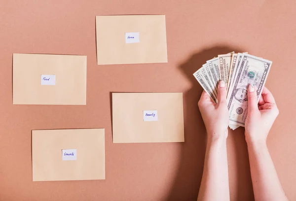 Kadın ellerinde dolar ve kahverengi arka planda para biriktirmek için yazıtlarla dolu zarflar. Para tasarruf kavramı