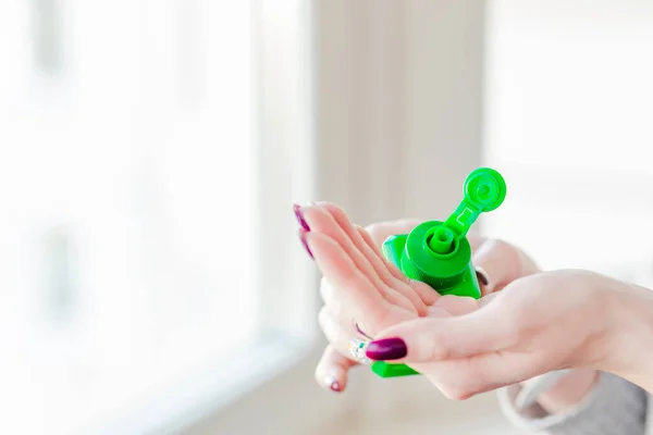 Girl disinfects hands with an antiseptic in a green bottle. Horizontal photo