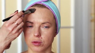 Makyaj sanatçısı bir kıza temeli fırçayla atar. Prosedür evde gerçekleşiyor. Video