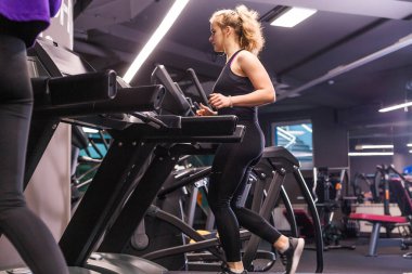 Siyah spor üniformalı bir kız spor salonundaki koşu bandında koşuyor. Yatay fotoğraf