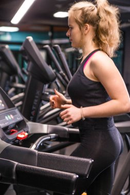 Siyah spor üniformalı bir kız spor salonundaki koşu bandında koşuyor. Vertycal fotoğraf