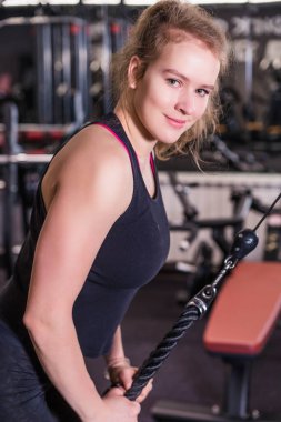 Spor kıyafetli atletik sarışın kadın spor salonunda trisepslerin üzerinde egzersiz yapıyor. Vertycal fotoğraf