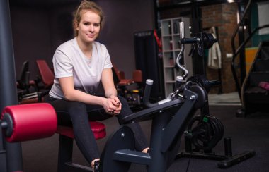 Sarışın vücut geliştiren kadın spor salonunda bankta oturuyor. Yatay fotoğraf
