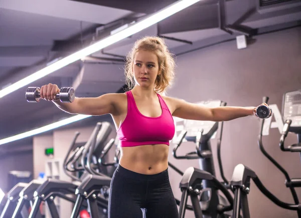 The girl does exercises with dumbbells in hands, trains hands in the gym. Horizontal photo