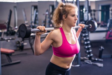Spor salonunda egzersiz yapan, omuzlarında halterle çömelme hareketleri yapan sağlıklı bir kadın. Yatay fotoğraf