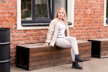 Güzel sarışın kız bankta oturuyor ve kameraya poz veriyor. Yatay fotoğraf