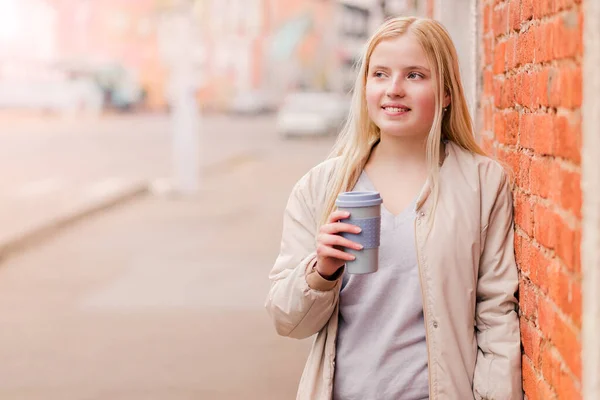 Portrait of young caucasian woman holding a cup of coffee against brick wall. Urban concept. — Stock Photo, Image