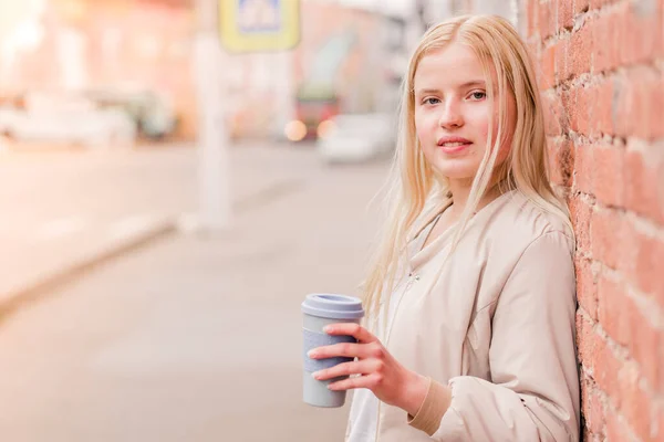 Portrait of young caucasian woman holding a cup of coffee against brick wall. Urban concept. — Stock Photo, Image