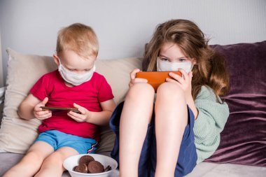 Beyaz çocuk ve kız çocuk koruyucu maske takıyor. Coronavirus Covid-19 ve hava kirliliğine karşı ev karantinasında birlikte oynuyorlar. Yatay fotoğraf