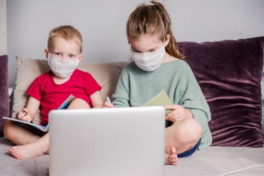 Çocuklar, CoVid-19 karantinası sırasında koruyucu bir maskeyle evde ders çalışırlar. Uzaktan öğrenmeyi dizüstü bilgisayarla öğrenirler. Bir erkek ve bir kız ödevlerini yaparlar. Yatay fotoğraf