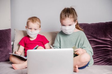 Çocuklar, CoVid-19 karantinası sırasında koruyucu bir maskeyle evde ders çalışırlar. Uzaktan öğrenmeyi dizüstü bilgisayarla öğrenirler. Bir erkek ve bir kız ödevlerini yaparlar. Yatay fotoğraf