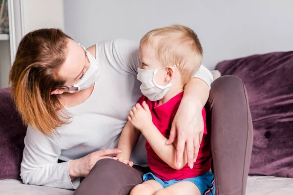 Mom and son in white medical masks look at each other. At home. Horizontal photo