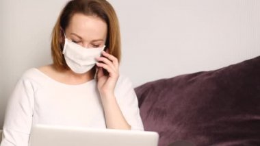 Evde dizüstü bilgisayarla çalışan, koruyucu maske takan genç bir iş kadını. Video