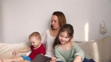 Genç anne, çocukları evde birlikte eğleniyor. Eğleniyor, şımartıyor, kanepede sarılıyor. Video