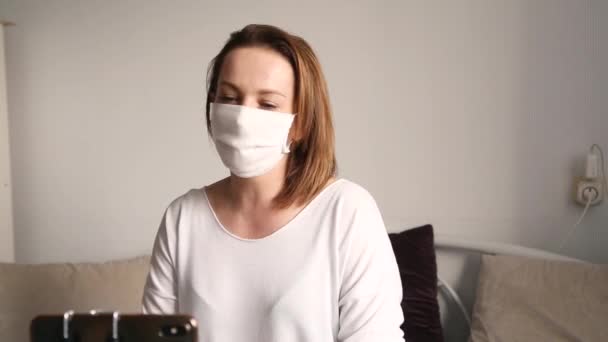 Uma Mulher Com Uma Máscara Médica Branca Olha Para Telefone — Vídeo de Stock