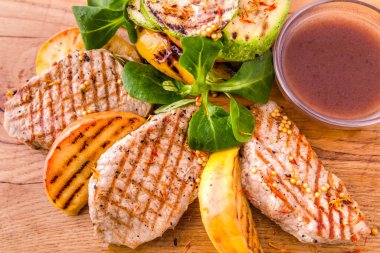 Beyaz arka planda ahşap bir tahtada ızgara domuz eti, elma ve kabak parçaları. Yatay fotoğraf