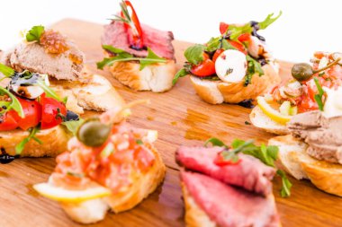 Beyaz arka planda tahta bir tahtanın üzerinde çeşitli bruschett 'ler vardı. Yatay fotoğraf