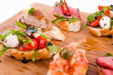 Beyaz arka planda tahta bir tahtanın üzerinde çeşitli bruschett 'ler vardı. Yatay fotoğraf