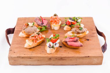 Beyaz arka planda tahta bir tahtanın üzerinde çeşitli bruschett 'ler vardı. Yatay fotoğraf