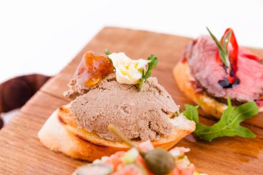 Beyaz arka planda tahta bir tahtanın üzerinde çeşitli bruschett 'ler vardı. Yatay fotoğraf