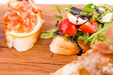 Beyaz arka planda tahta bir tahtanın üzerinde çeşitli bruschett 'ler vardı. Yatay fotoğraf