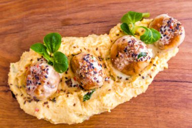 Tahta tepside susam tohumları, kırmızı ekmek ve yeşillikler serpiştirilmiş darı lapası serpiştirilmiş köfteler ya da köfteler. Yatay fotoğraf