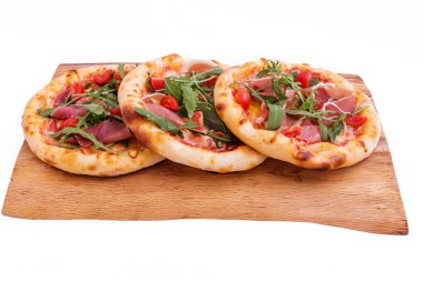 Jambonlu üç pizza, domates, ahşap tepside roka. Nesne beyaz bir arkaplanda izole edilmiştir. Yatay fotoğraf