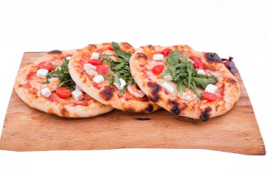 Tahta tepside karidesli, domatesli, roka ve peynirli üç pizza. Nesne beyaz bir arkaplanda izole edilmiştir. Yatay fotoğraf