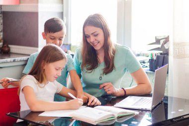 Anne ve kızı birlikte ders alıp dizüstü bilgisayara bakıyorlar. Oğlum, küçük kardeş arkada durup izliyor. Yatay fotoğraf