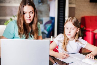 Anne ve kızı birlikte ders alıp dizüstü bilgisayara bakıyorlar. Yatay fotoğraf