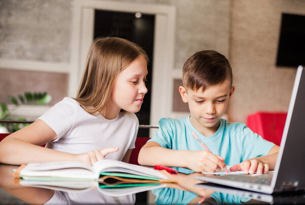 Boy and girl, brother and sister study at home. Older sister helps younger brother do homework. Horizontal photo
