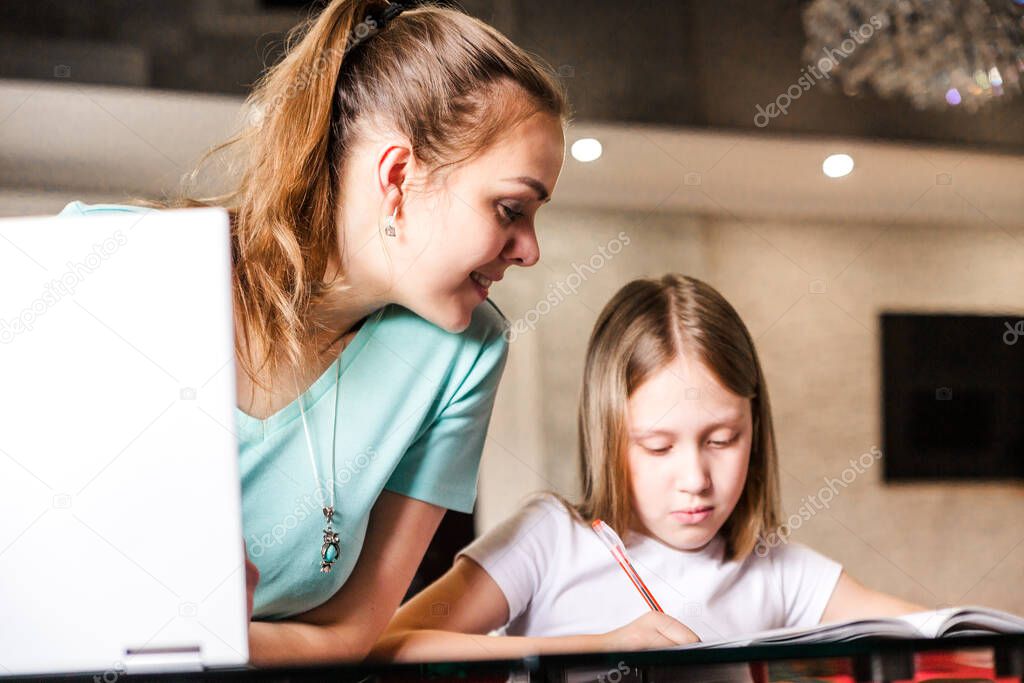 Mom and daughter do school lessons together. Mom looks in the daughter's notebook. Horizontal photo