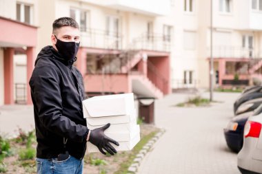 Siyah üniformalı, siyah koruyucu maskeli ve eldivenli teslimatçı eve beyaz kutularda yiyecek getiriyor.. 
